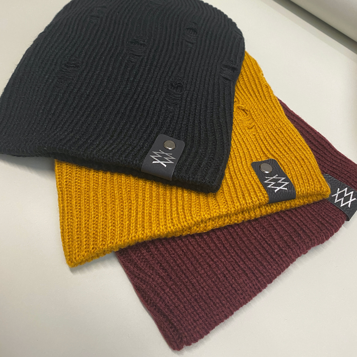 Three layered beanies in black, mustard, and burgundy, each showcasing the DUUW WUUD logo on the edge.