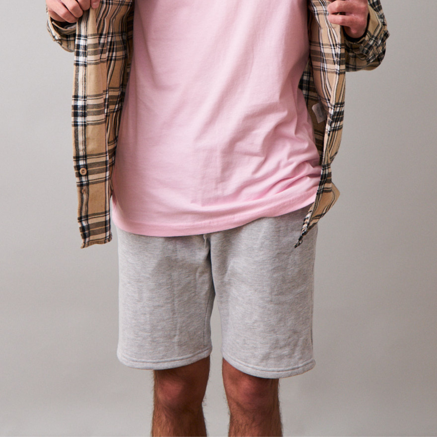 close up of man wearing long sleeve beige flannel, pink tshirt underneath and gray jogger shorts
