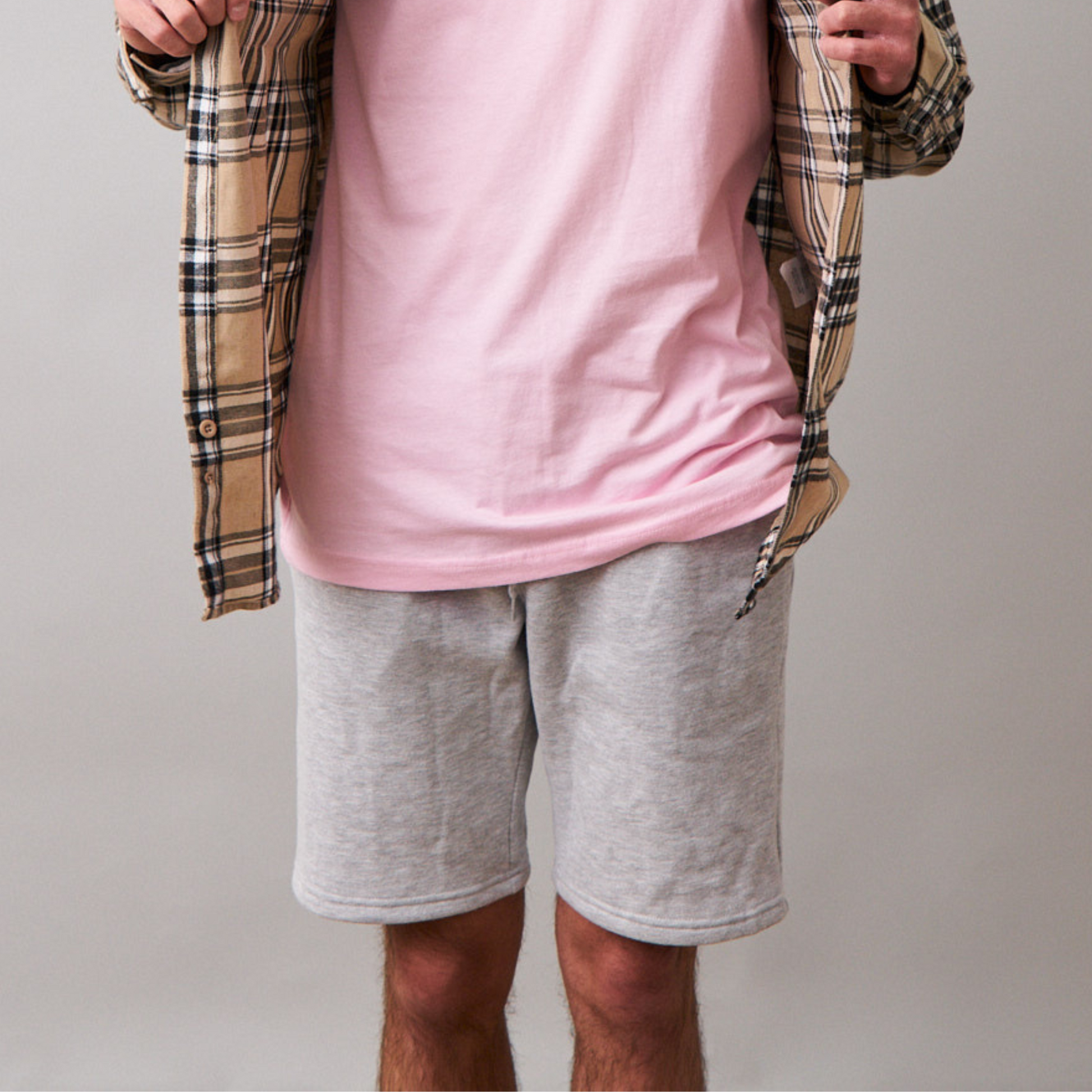 close up of man wearing long sleeve beige flannel, pink tshirt underneath and gray jogger shorts