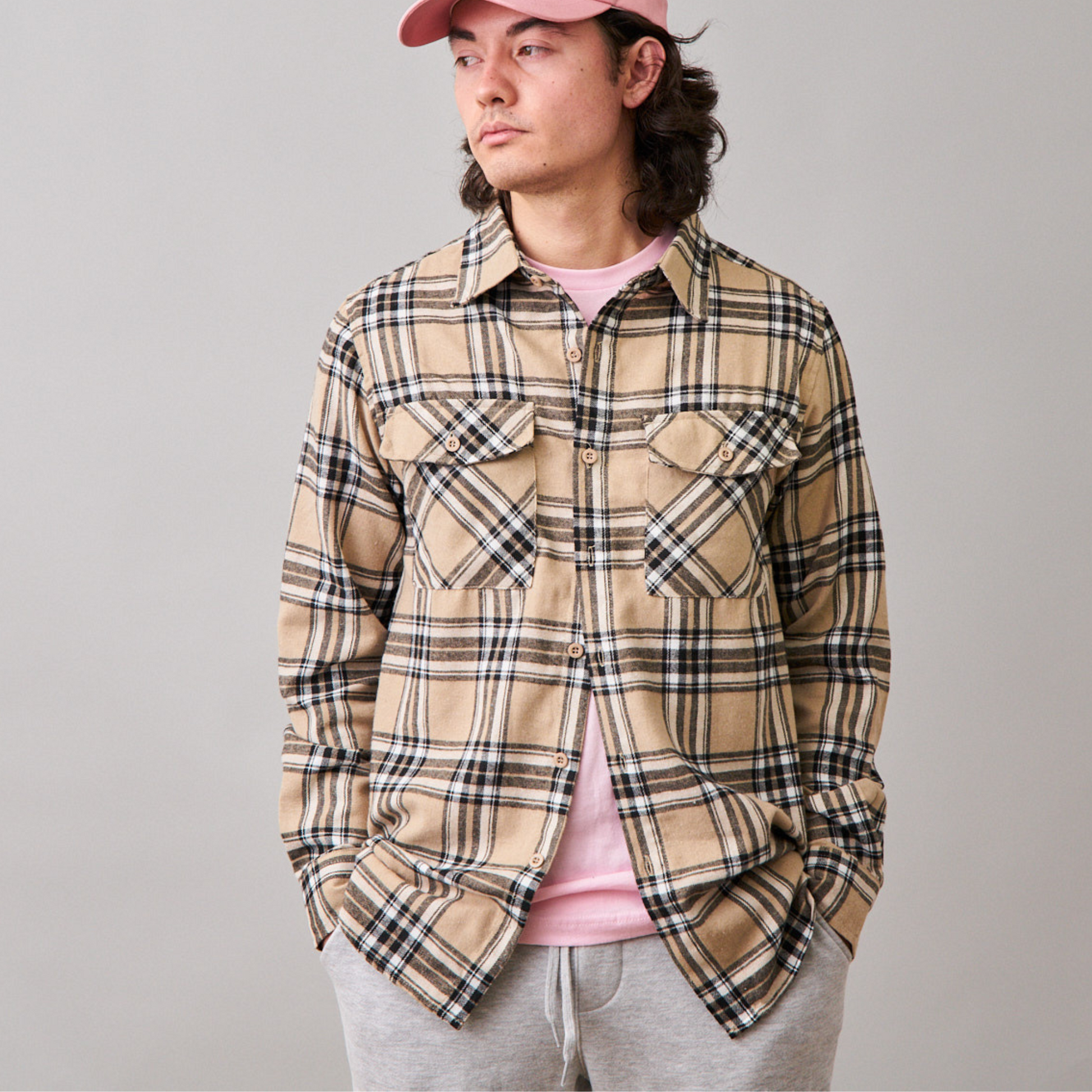 man wearing long sleeve beige flannel, pink tshirt underneath, pink dad cap and grey jogger shorts